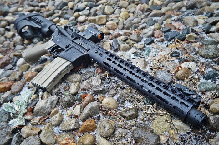 AR-15 rifle with red dot sight on stones