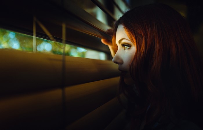 Woman with red hair peeking through blinds