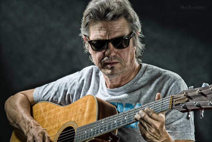 Gerry Wall playing acoustic guitar wearing sunglasses