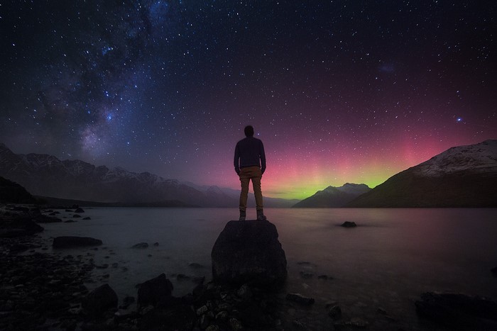 Man watching Aurora Australis and Milky Way over mountains