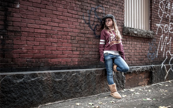 Girl in jeans and sweatshirt leaning against brick wall