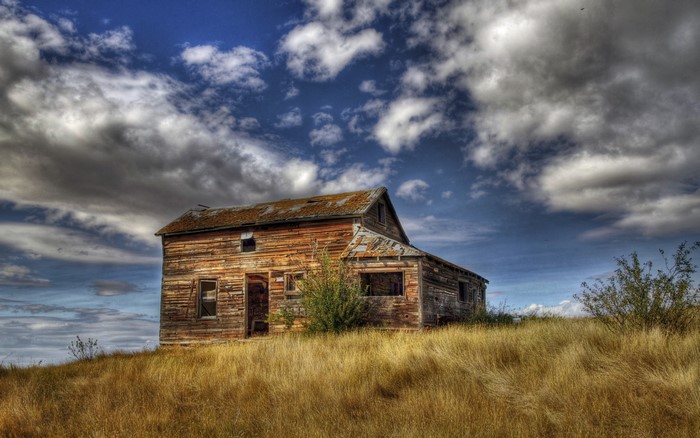 Abandoned wooden house on a grassy hill under a cloudy sky