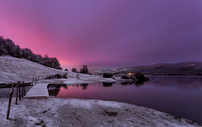 Snowy landscape with a wooden pier and a lake at sunset