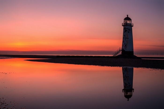 Lighthouse reflecting in water at sunset