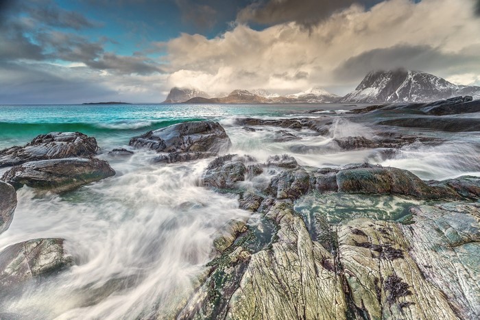Waves crashing on rocky shore with mountains in background