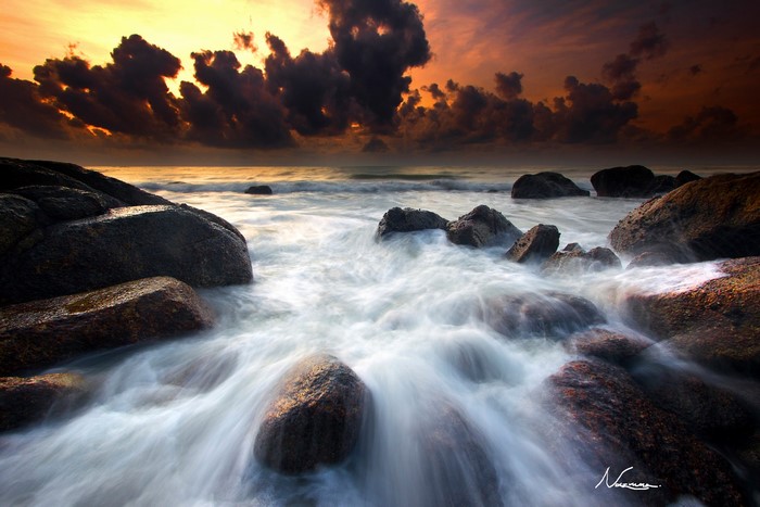 Ocean waves crashing on rocks at sunset with dark clouds