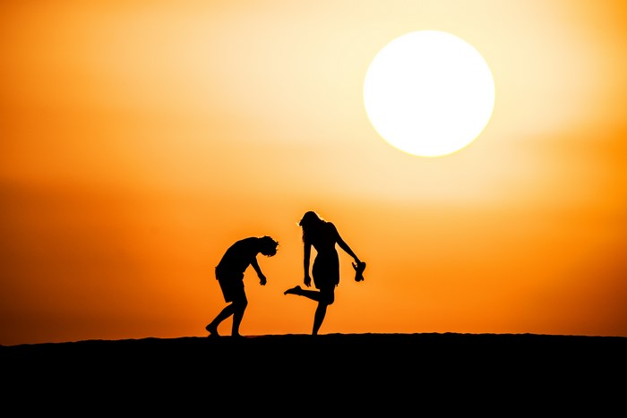 Silhouettes of two people against a bright sunset