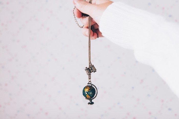 Hand holding a necklace with a globe pendant