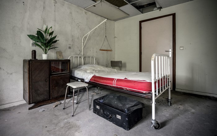Abandoned hospital room with bed and suitcase