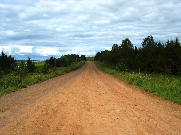 Dirt road through a rural landscape with trees and clouds
