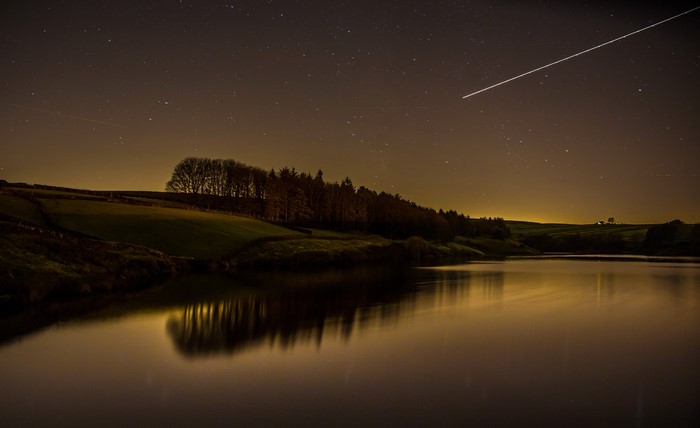 Night sky over a lake with a contrail
