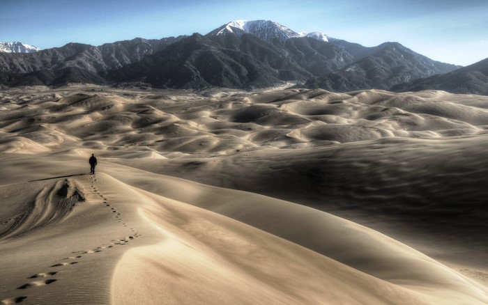 Person walking on sand dunes with mountains in background