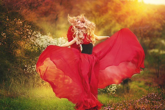 Blonde girl in a red dress dancing in a field