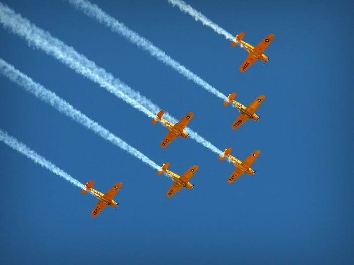 Six yellow airplanes flying in formation with smoke trails
