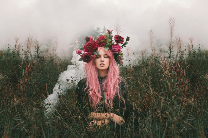 Woman with pink hair and flower crown in grass with smoke