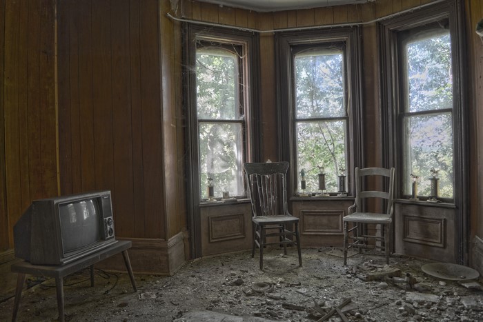 Old TV and chairs in abandoned room with windows