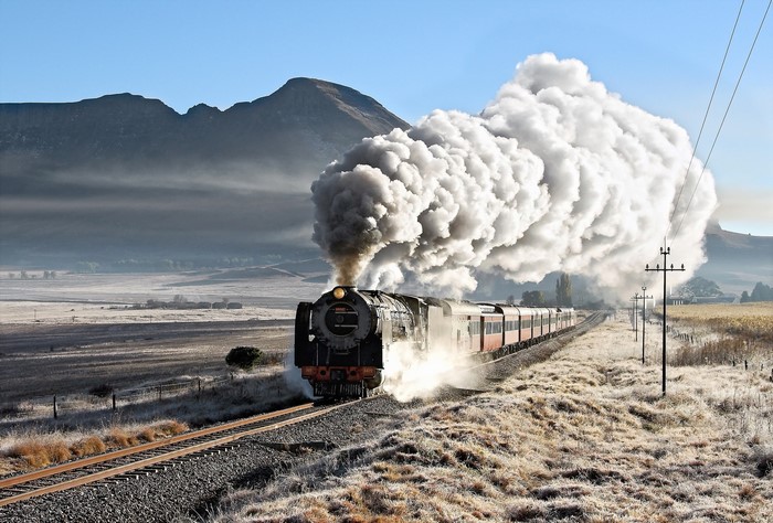 Steam train billowing smoke through a misty mountain landscape