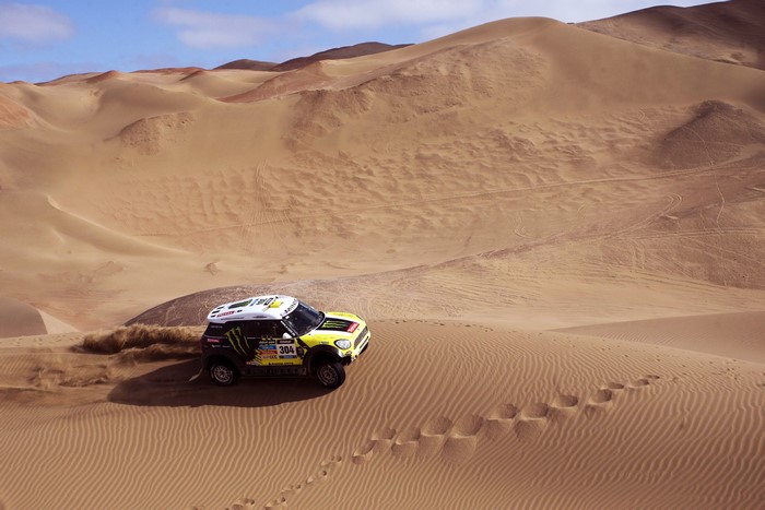 Mini Cooper Dakar X-raid car driving through desert dunes
