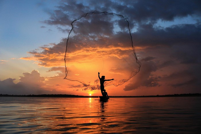 Fisherman casting net at sunset in Thailand