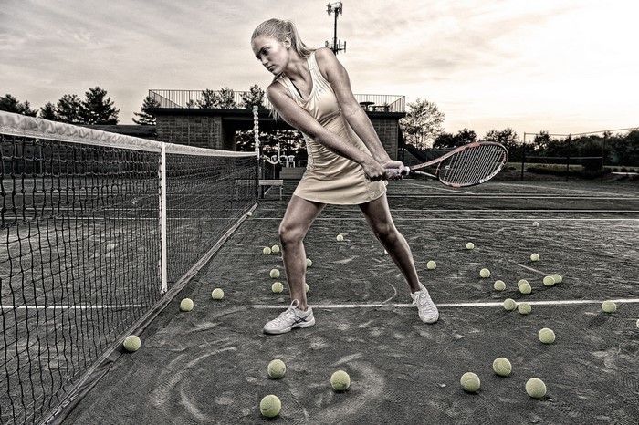 Young woman playing tennis on a court with many balls