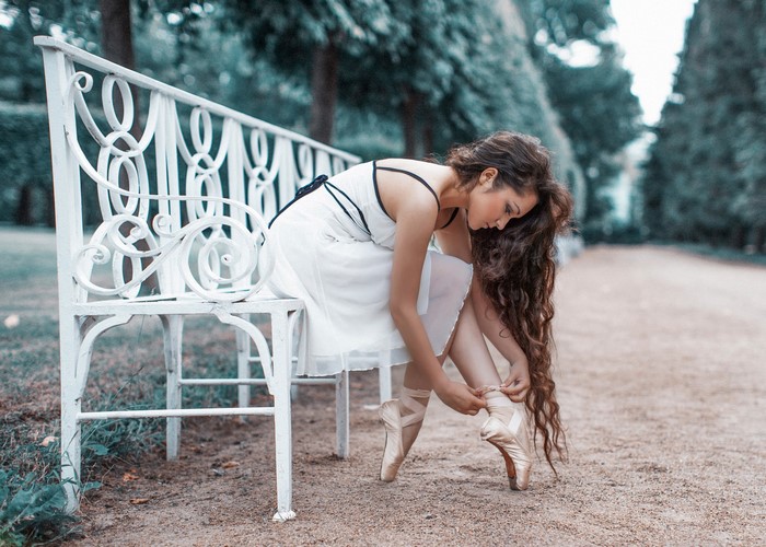 Ballerina tying pointe shoes on a park bench