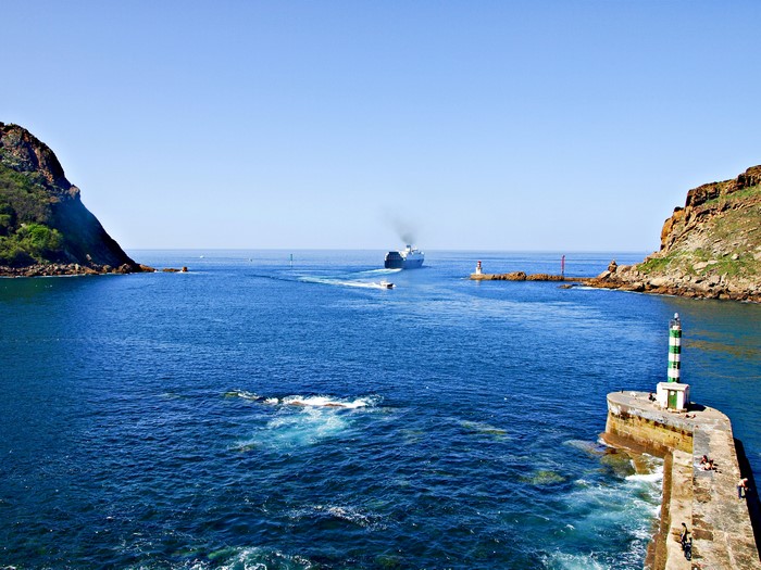 Cruise liner entering a harbor with lighthouses and rocky cliffs