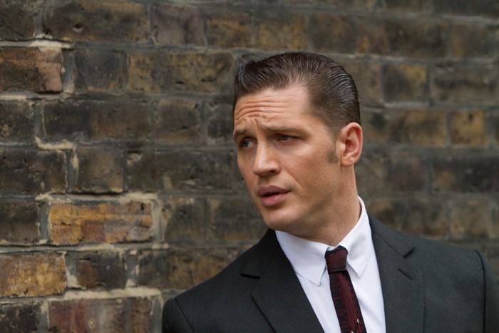 Tom Hardy in a suit standing by a brick wall