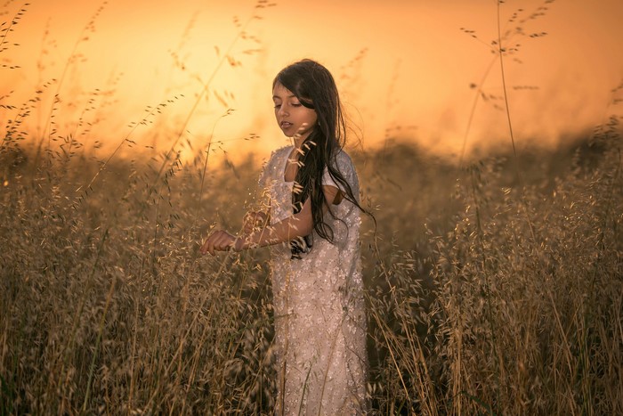 Young girl in a field of tall grass at sunset