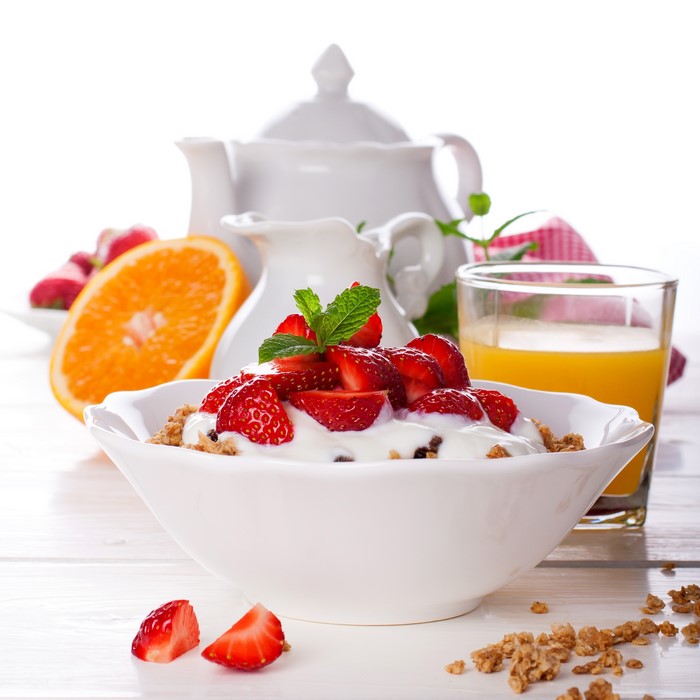 Bowl of muesli with strawberries and yogurt, orange juice, and teapot