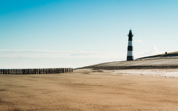 Lighthouse on a sandy beach with wooden posts