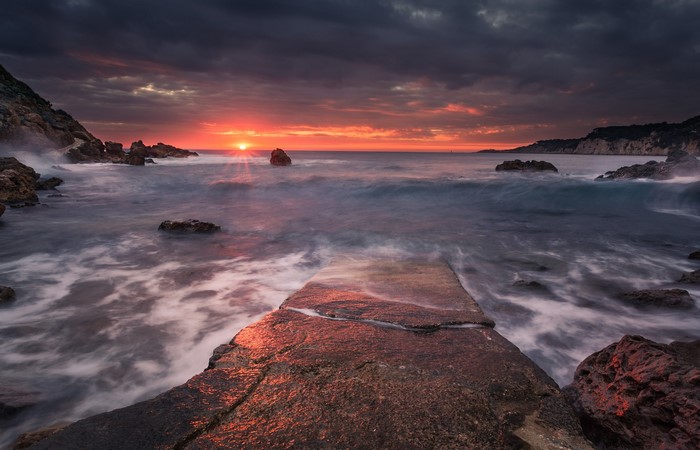 Sunset over the sea with rocky coast and pier