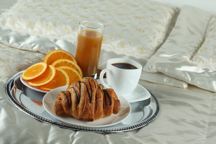 Breakfast tray with croissant, coffee, orange slices, and juice