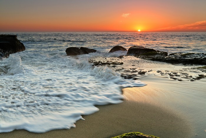 Sunset over the ocean with waves crashing on rocks