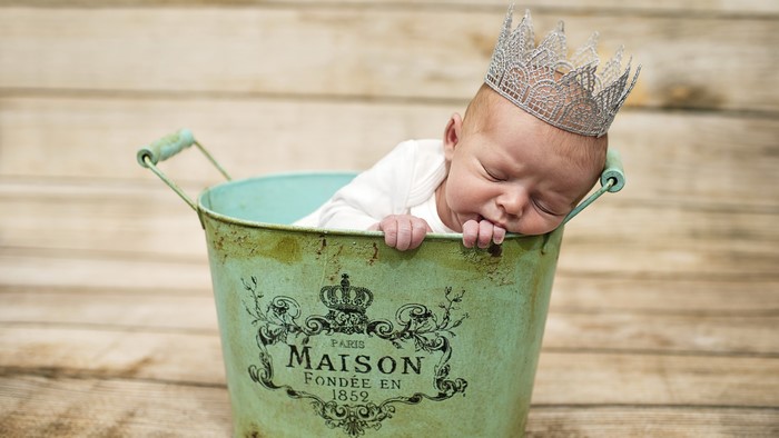 Baby wearing a crown sleeping in a bucket