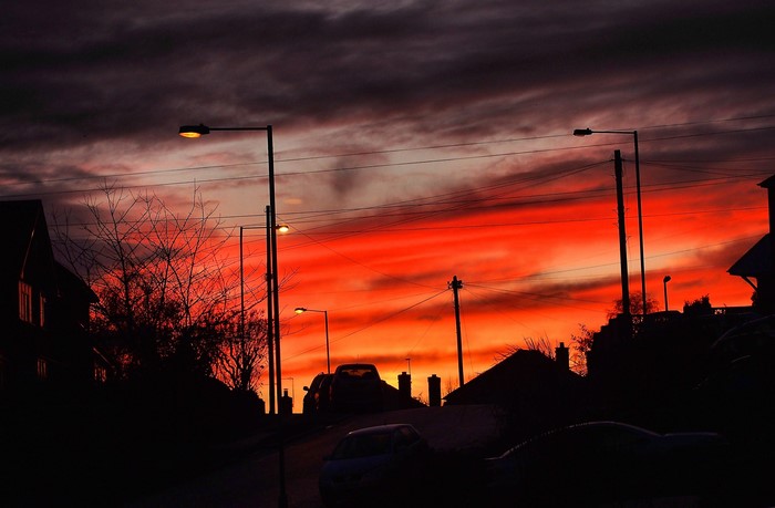 Fiery sunset over a suburban street with silhouetted houses and streetlights