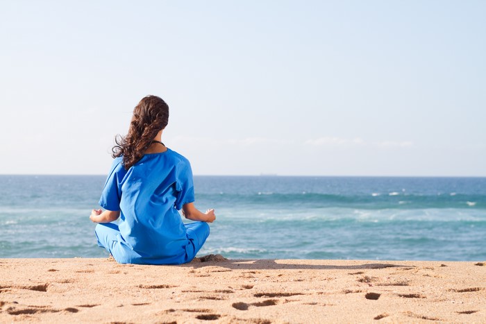 Woman in blue scrubs meditating on beach