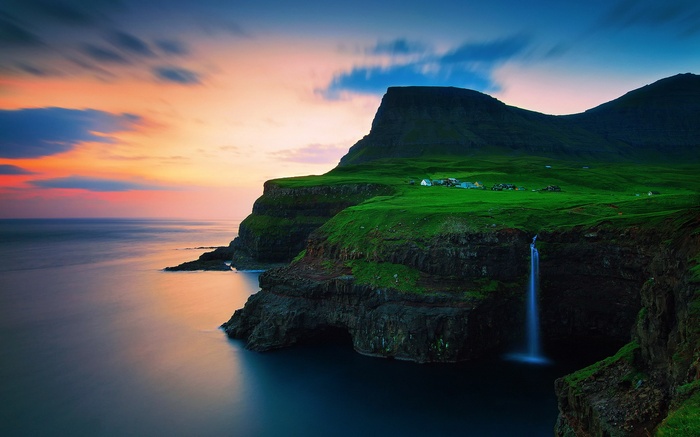 Waterfall cascading from a grassy cliff into the ocean at sunset