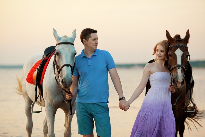 Couple with horses on a beach at sunset