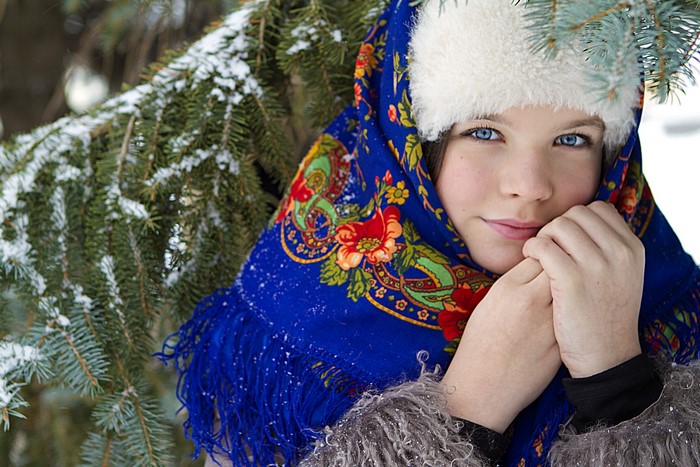 Girl in traditional Russian attire near a snowy fir tree