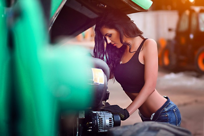 Brunette girl in singlet and jeans working on engine