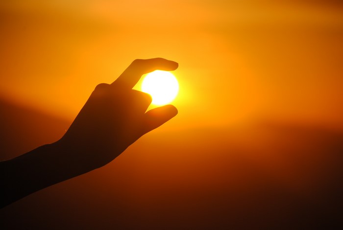 Silhouette of a hand holding the sun at sunset