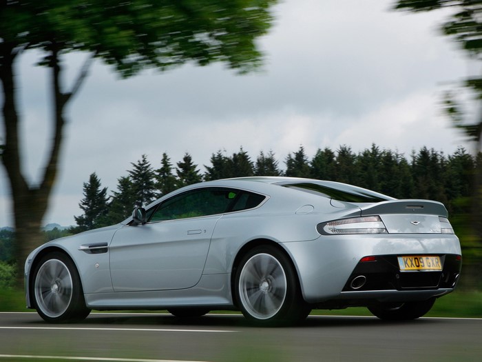 Silver Aston Martin V12 Vantage driving on a road