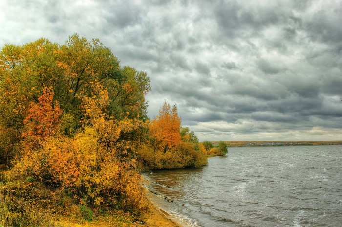Autumn trees on the shore of a wide river under a cloudy sky