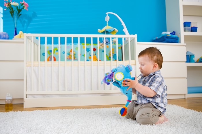 Baby boy playing with a toy near a crib