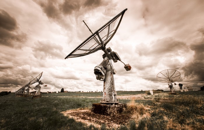 Abandoned Satellite Dishes in a Field Under Cloudy Sky
