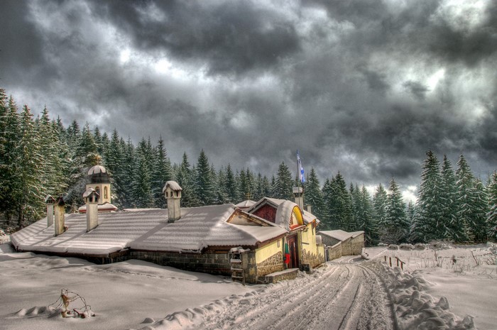 Snowy monastery in a pine forest under stormy clouds