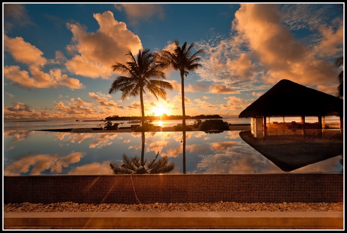 Sunset over the ocean with palm trees and a hut