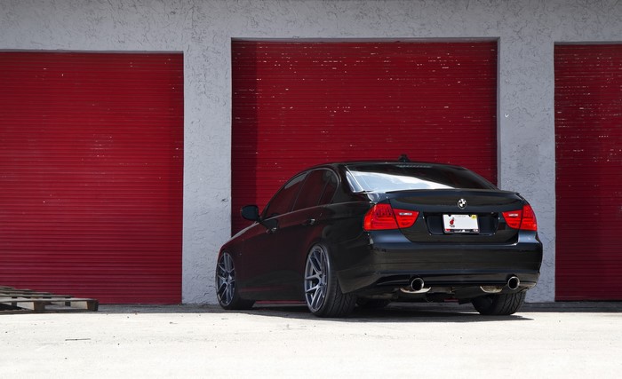 Black BMW E90 sedan parked in front of red garage doors
