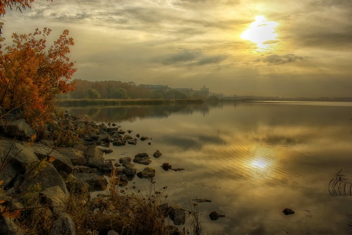 Autumn riverbank with sunlit sky and distant buildings