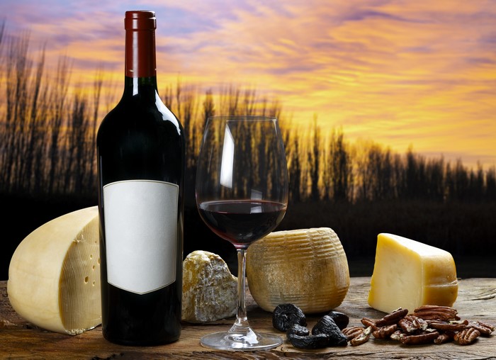 Wine bottle and glass with cheese and nuts at sunset